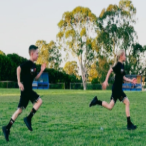 Two people running on a grassy field with trees in the background